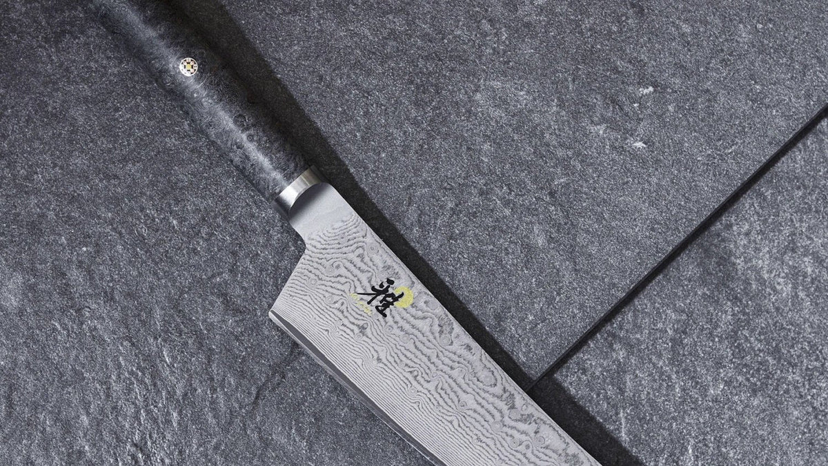 Miyabi 5000MCD Damastmesser mit gemusterter Klinge und Holzgriff auf einem Schneidebrett