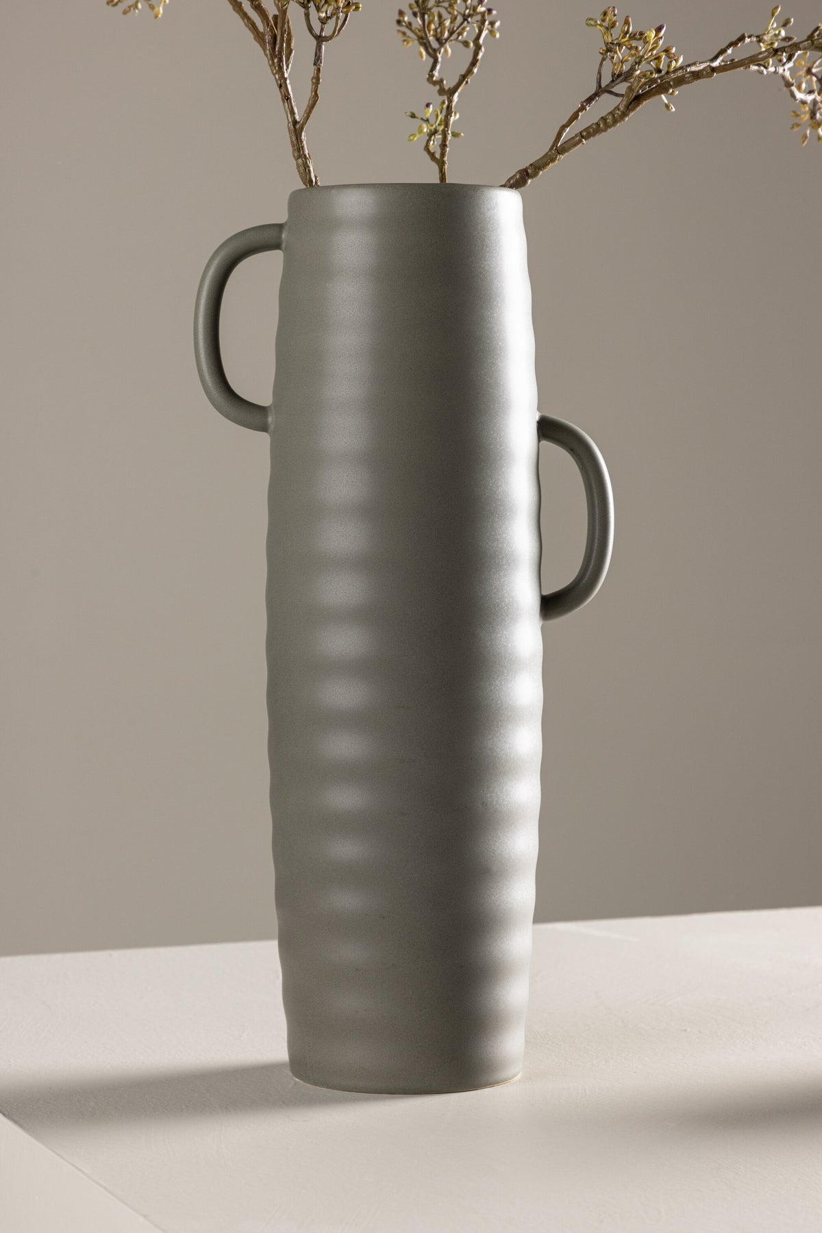 Beige Cent Vase von Venture Home aus Steinzeug mit wellenförmiger Struktur und zwei asymmetrisch angebrachten Griffen an den Seiten.