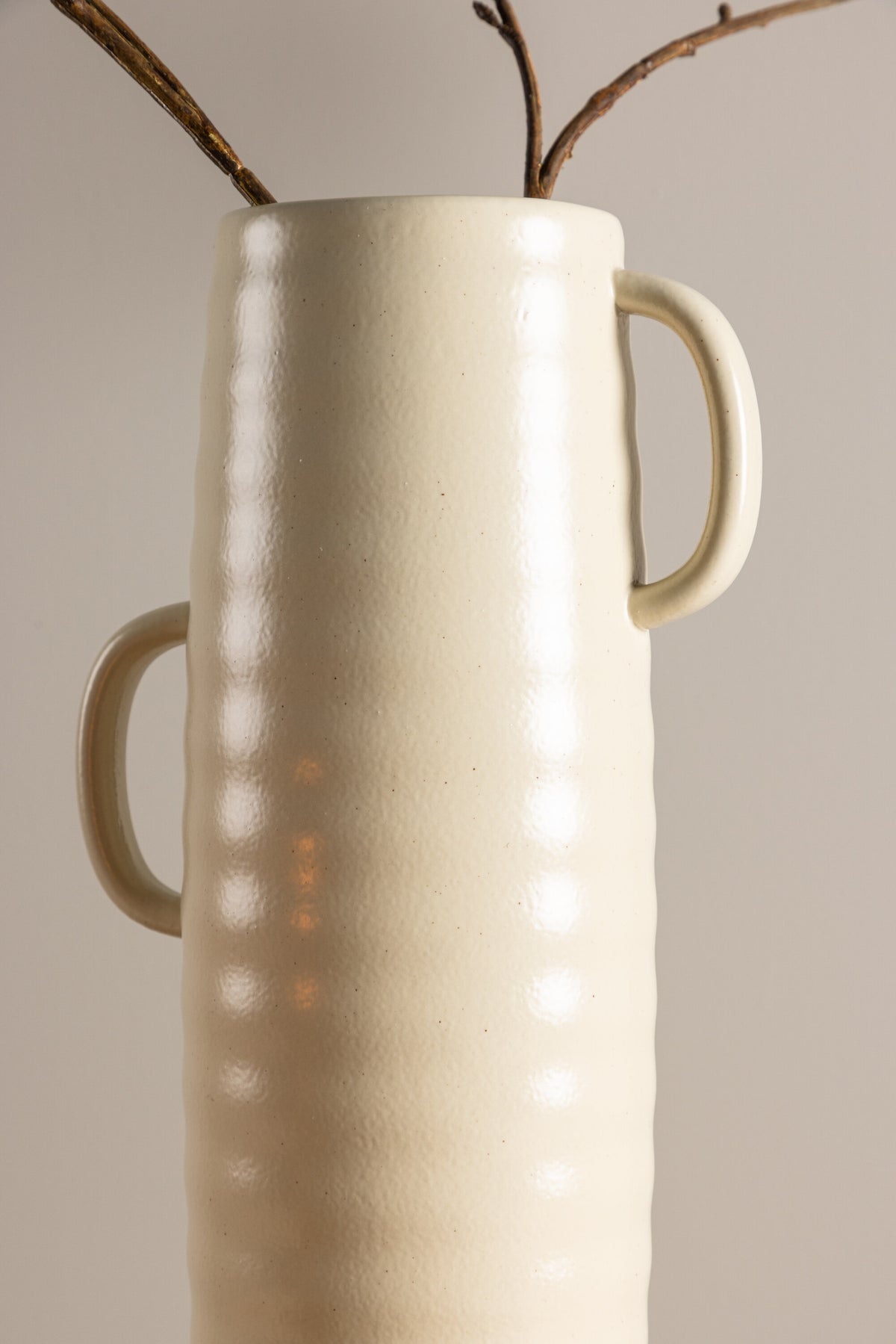 Beige Cent Vase von Venture Home aus Steinzeug mit wellenförmiger Struktur und zwei asymmetrisch angebrachten Griffen an den Seiten.