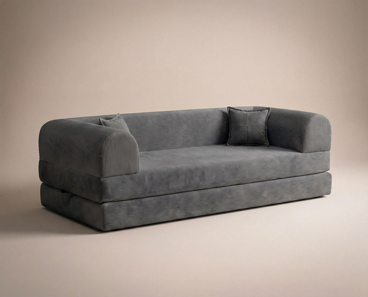 Anthrazitfarbenes 3-Sitzer Schlafsofa aus geripptem Cord-Plüschstoff mit zwei Kissen und sichtbarer rutschfester Sohle.