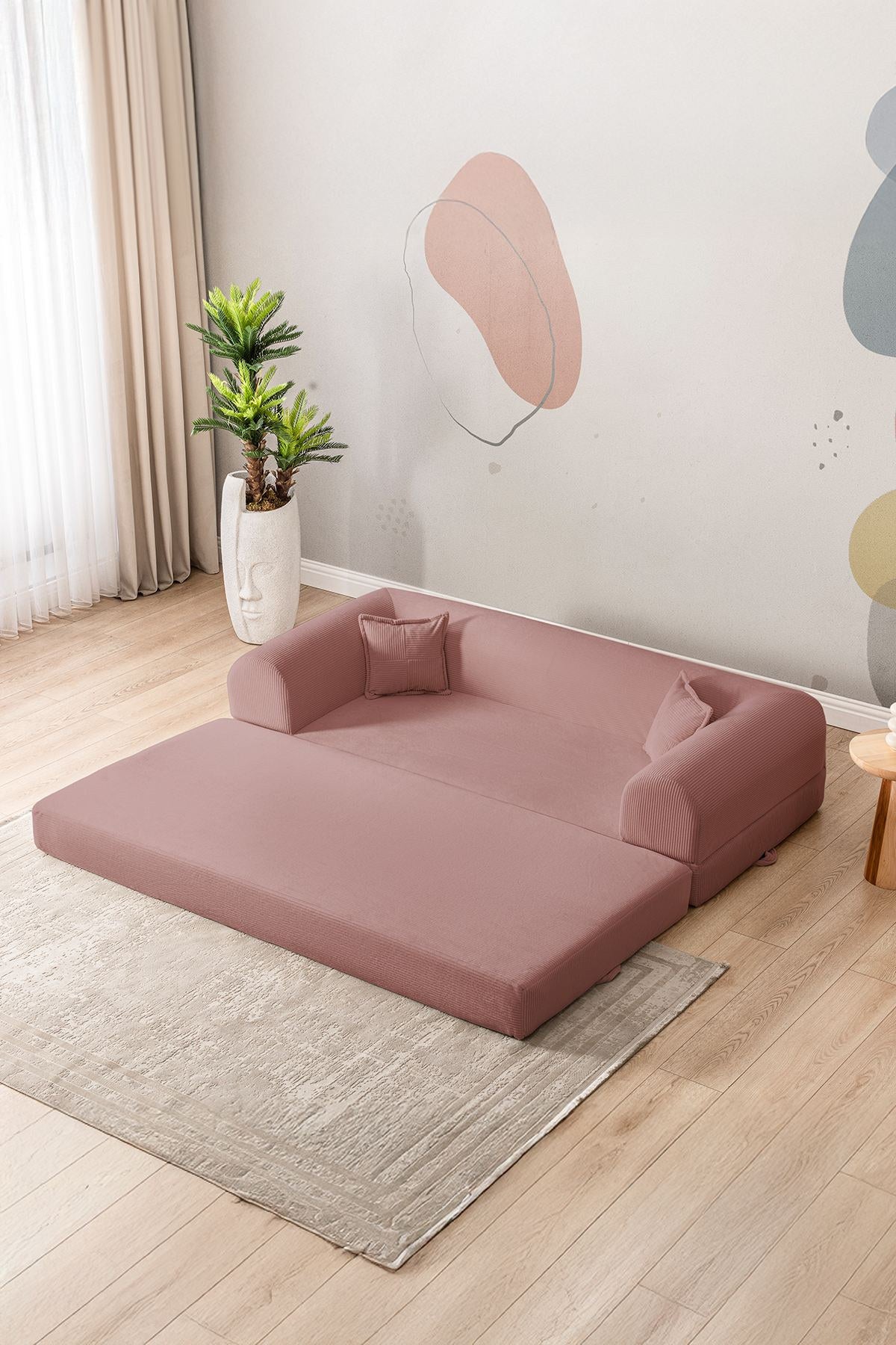 Rosafarbenes 3-Sitzer Schlafsofa aus geripptem Cord-Plüschstoff mit zwei Kissen und rutschfester Sohle, Frontalansicht auf hellem Hintergrund.