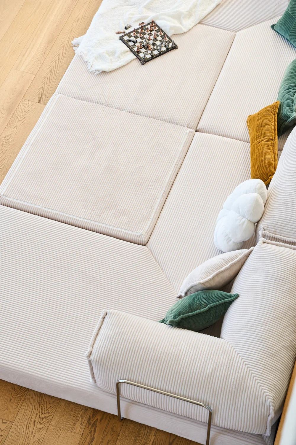 Cremefarbenes Eck-Schlafsofa aus Cord-Plüschstoff mit vier Kissen, rutschfester Sohle und abnehmbarem Bezug, Frontalansicht auf hellem Untergrund.