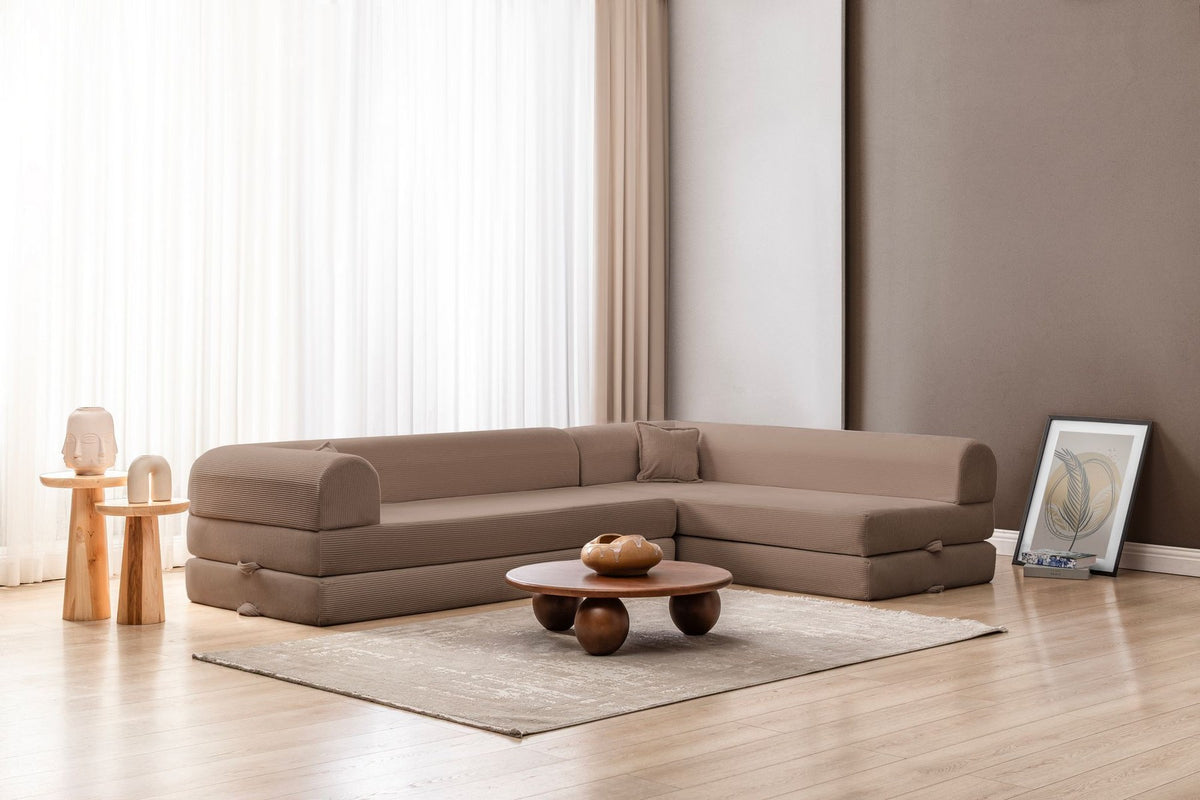 Beiges Ecksofa-Bett aus Cord-Plüschstoff mit vier passenden Kissen, L-Form, sichtbare Naht der abnehmbaren Bezugsstoffe auf niedrigem Sockel.