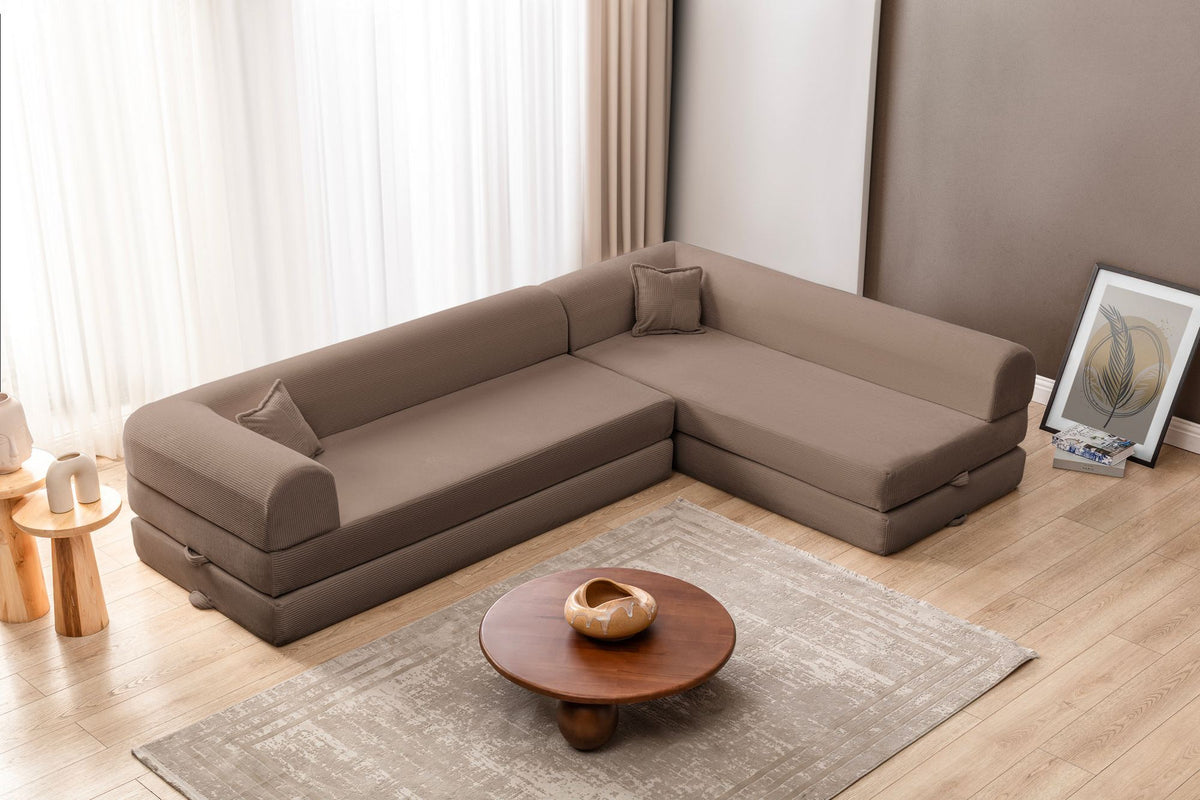 Beiges Ecksofa-Bett aus Cord-Plüschstoff mit vier passenden Kissen, L-Form, sichtbare Naht der abnehmbaren Bezugsstoffe auf niedrigem Sockel.