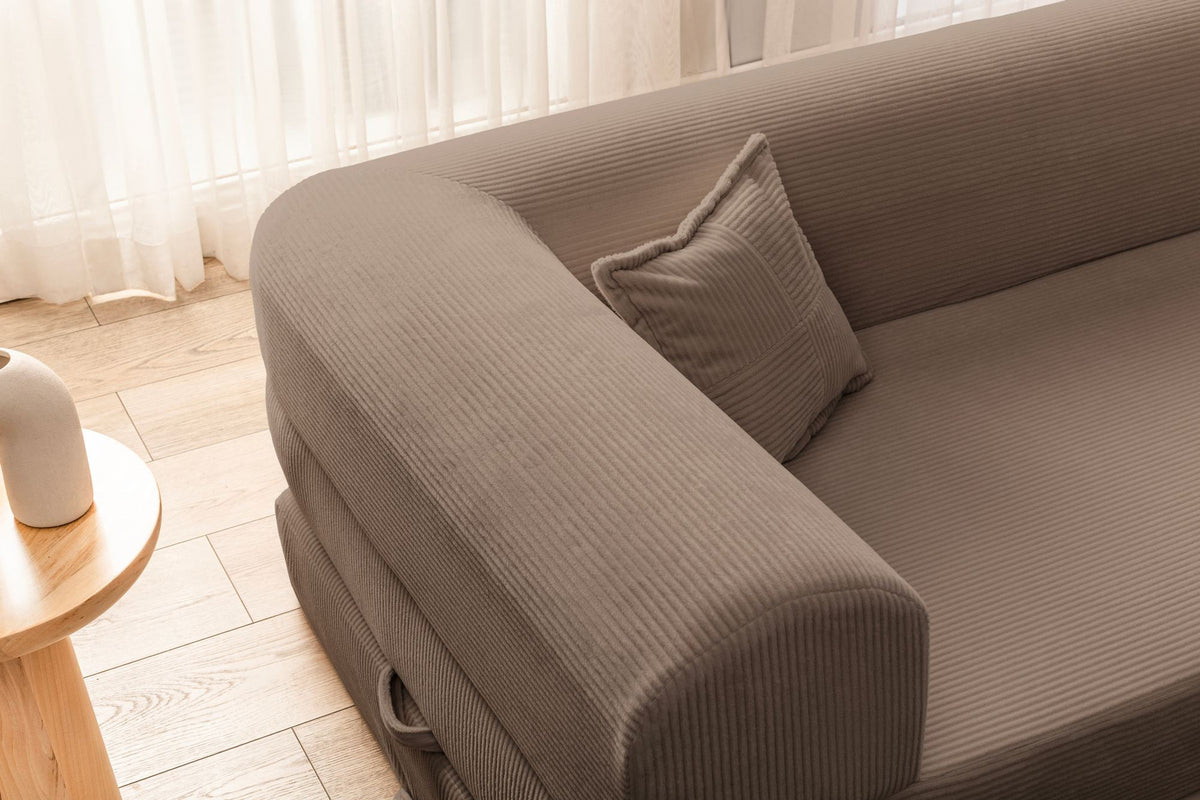 Beiges Ecksofa-Bett aus Cord-Plüschstoff mit vier passenden Kissen, L-Form, sichtbare Naht der abnehmbaren Bezugsstoffe auf niedrigem Sockel.
