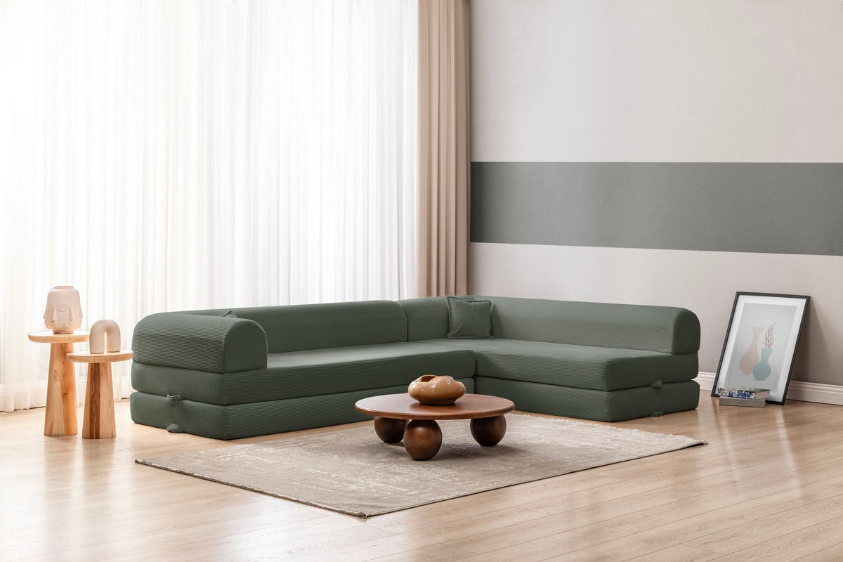 Grünes Ecksofa-Bett aus geripptem Cord-Plüschstoff mit vier Kissen, Rückenlehne und Sitzfläche aus Schaumstoff, Frontalansicht.