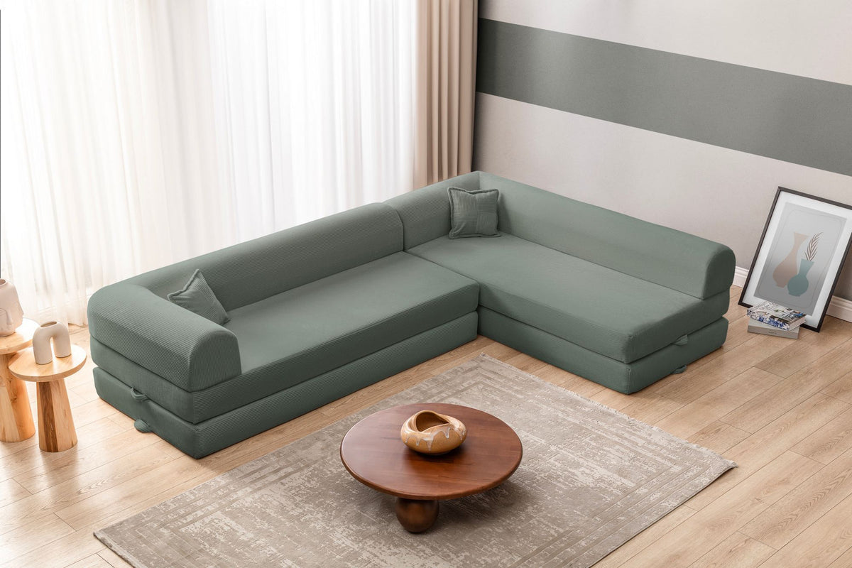Grünes Ecksofa-Bett aus geripptem Cord-Plüschstoff mit vier Kissen, Rückenlehne und Sitzfläche aus Schaumstoff, Frontalansicht.