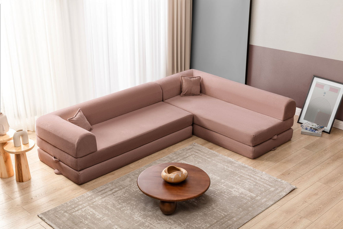 Rosa Ecksofa-Bett aus Cord-Plüschstoff mit vier Kissen, breiter Sitzfläche und niedriger Rückenlehne, als Sofa und Bett nutzbar.
