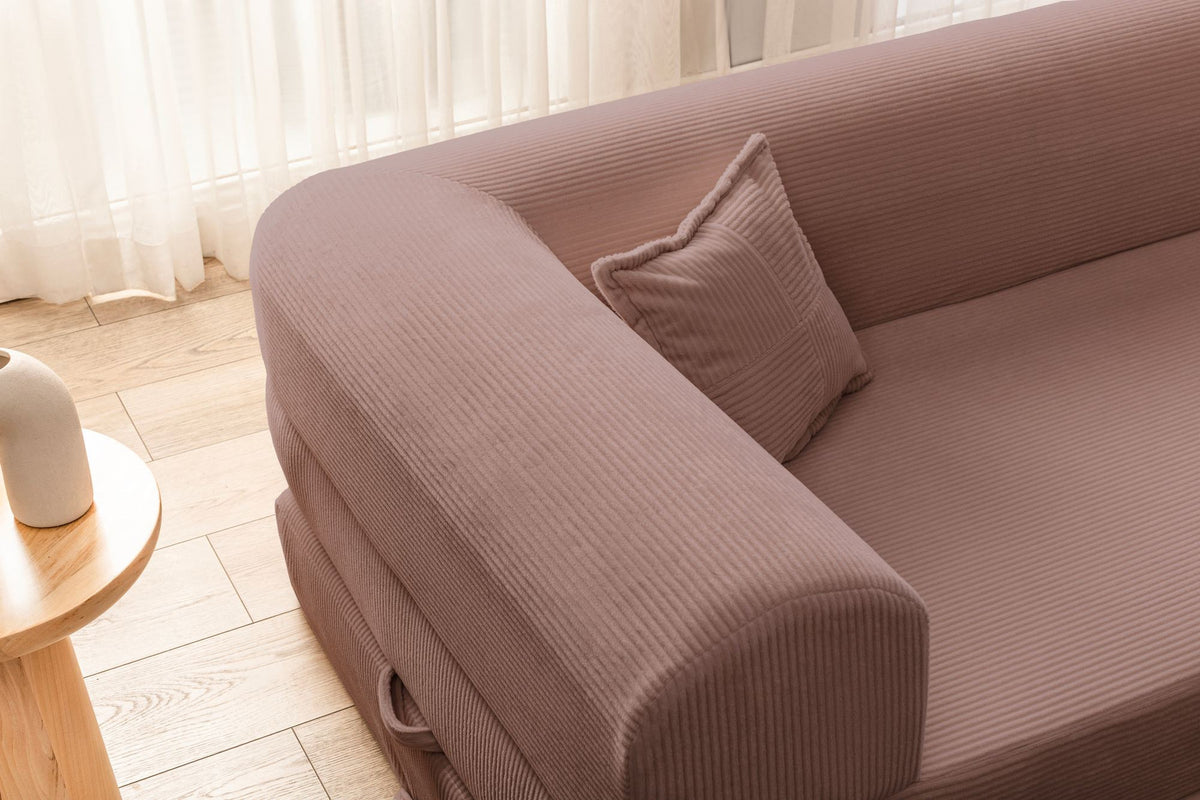 Rosa Ecksofa-Bett aus Cord-Plüschstoff mit vier Kissen, breiter Sitzfläche und niedriger Rückenlehne, als Sofa und Bett nutzbar.