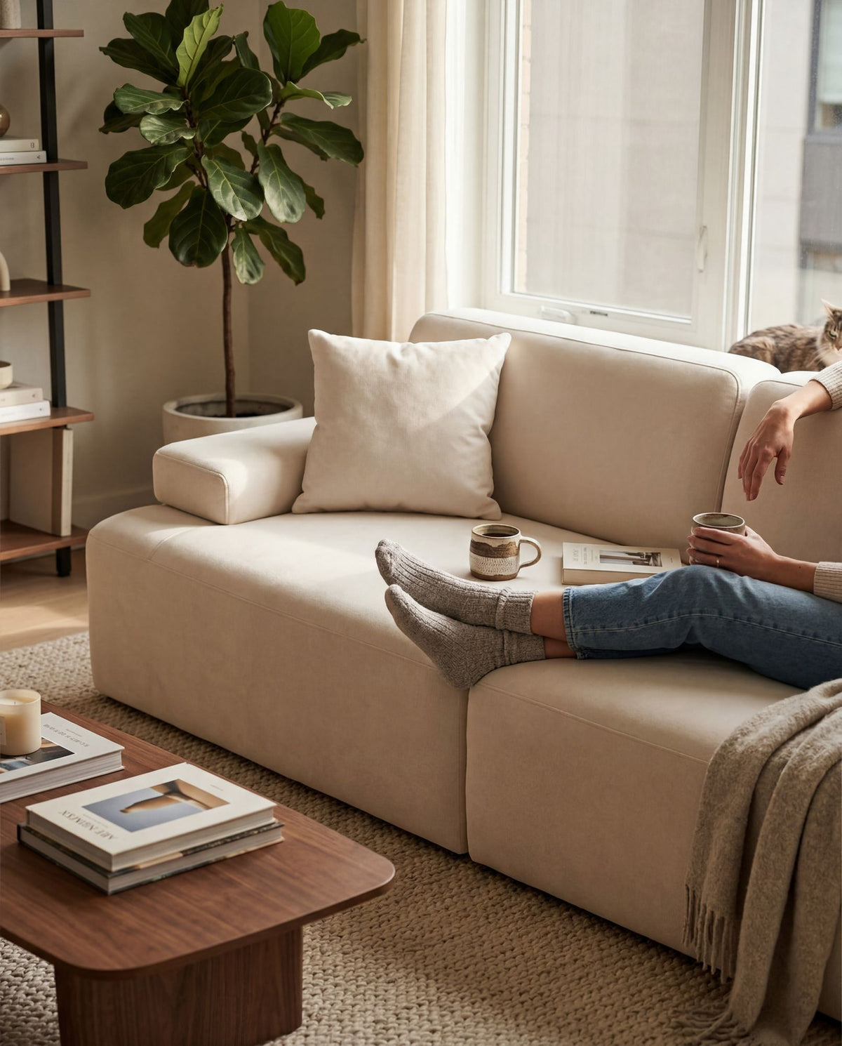 Cremefarbenes 3-Sitzer Sofa aus Polyesterstoff mit Buchenholzgestell, niedrigen Kunststoffbeinen und zwei Kissen.