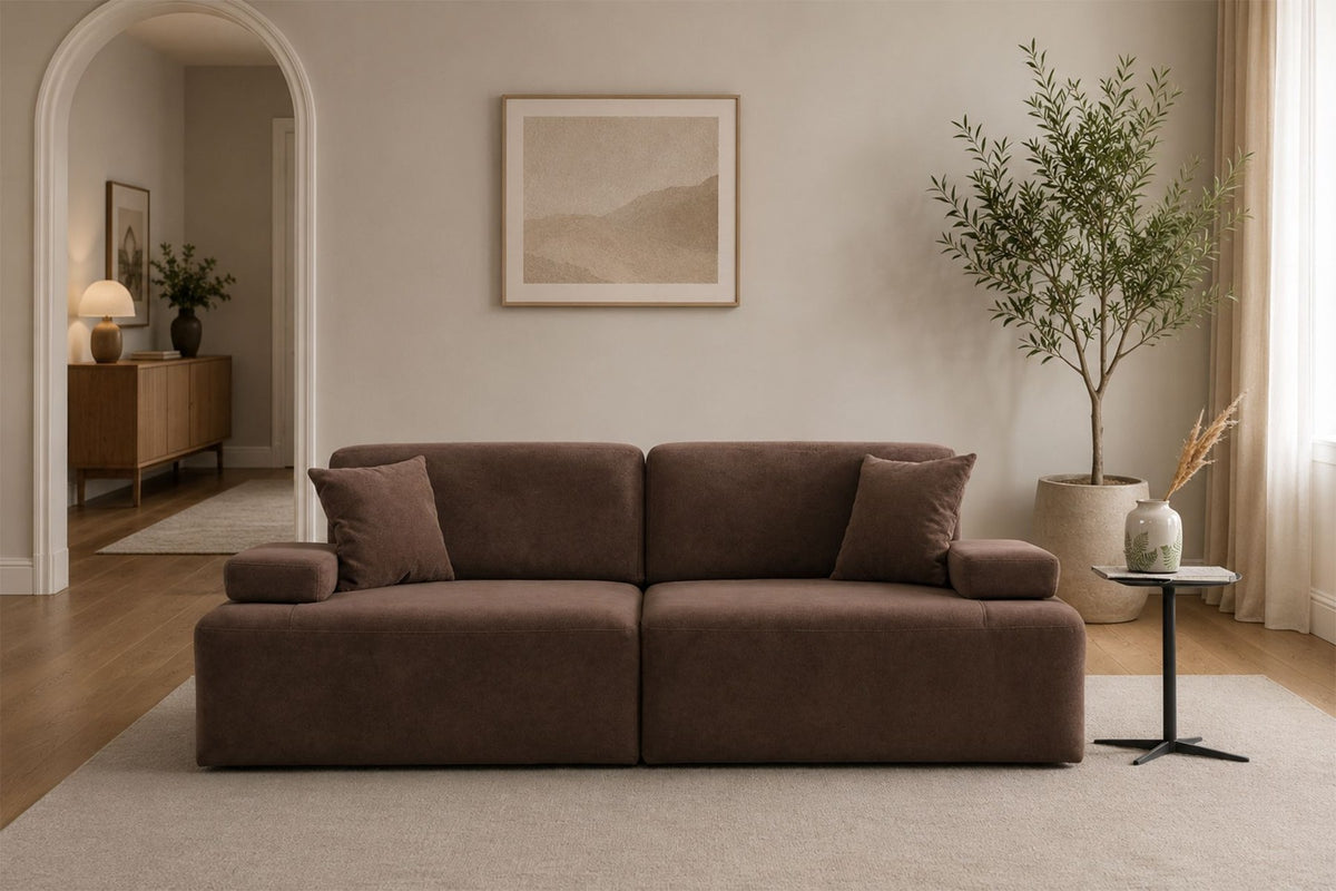 Braunes 3-Sitzer Sofa Madlen von Hanah Home mit niedrigen Kunststoffbeinen, Polyesterbezug, zwei Kissen und sichtbarem Gestell aus Buchenholz.
