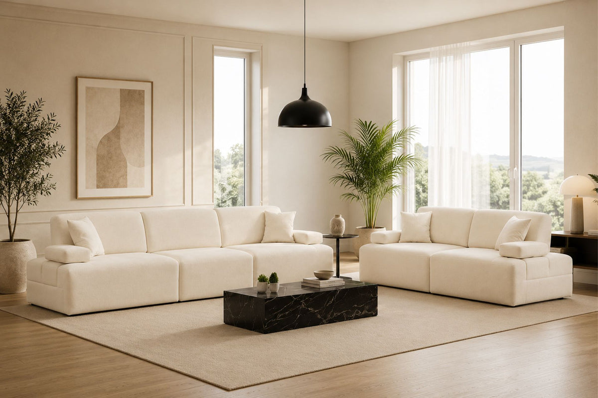 Cremefarbenes Madlen 4-Sitzer Sofa von Hanah Home mit niedrigen Kunststoffbeinen, Polyesterbezug und zwei Kissen auf hellem Untergrund.