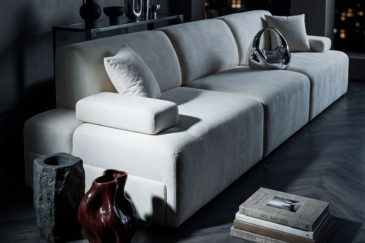 Cremefarbenes Madlen 4-Sitzer Sofa von Hanah Home mit niedrigen Kunststoffbeinen, Polyesterbezug und zwei Kissen auf hellem Untergrund.