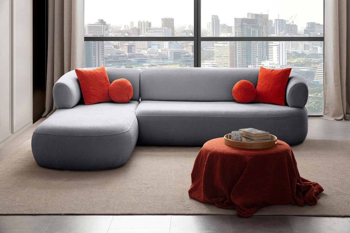 Graues Ecksofa links mit Boucle-Stoffbezug, Gestell aus Hainbuche und Spanplatte, Kunststoffbeinen und vier losen Kissen im Wohnzimmer.