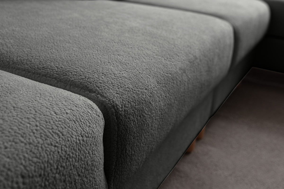 Anthrazitfarbenes Eck-Schlafsofa mit Coco-Boucle-Stoffbezug, Holzbeinen und rechter Truhe, fotografiert freistehend im Raum.