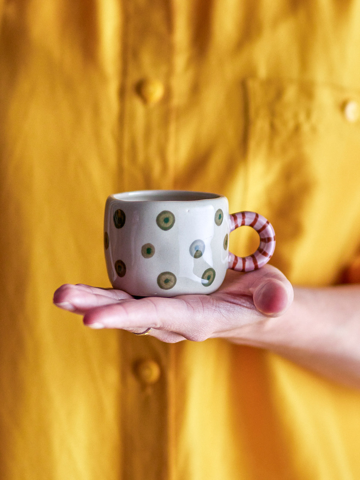 Weisse Nini Tasse aus Steingut von Bloomingville mit handbemaltem Muster, kleine runde Form mit Henkel, auf hellem Hintergrund fotografiert.