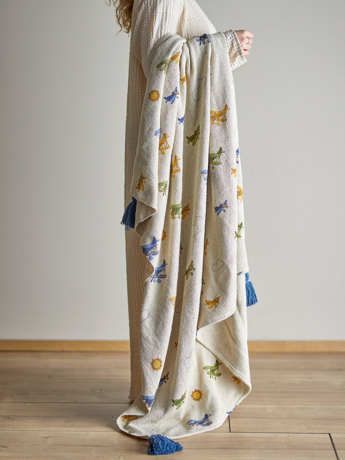 Weisse Wolldecke der Serie Plane von Bloomingville Mini aus Baumwolle, Polyester und Viskose, bedruckt mit Flugzeug- und Wolkenmotiv, blaue Quasten an den Ecken.