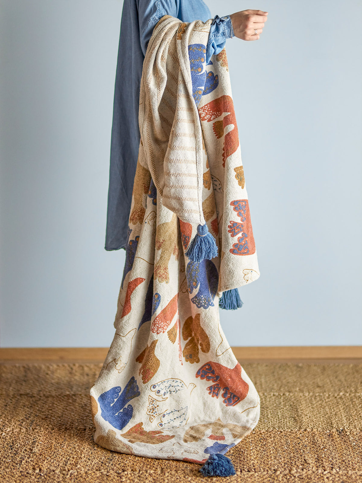 Wolldecke Anniversary von Bloomingville in Braun mit buntem botanischem Druckmuster, aus Baumwolle, Polyester und Viskose, mit blauen Quasten an den Ecken.