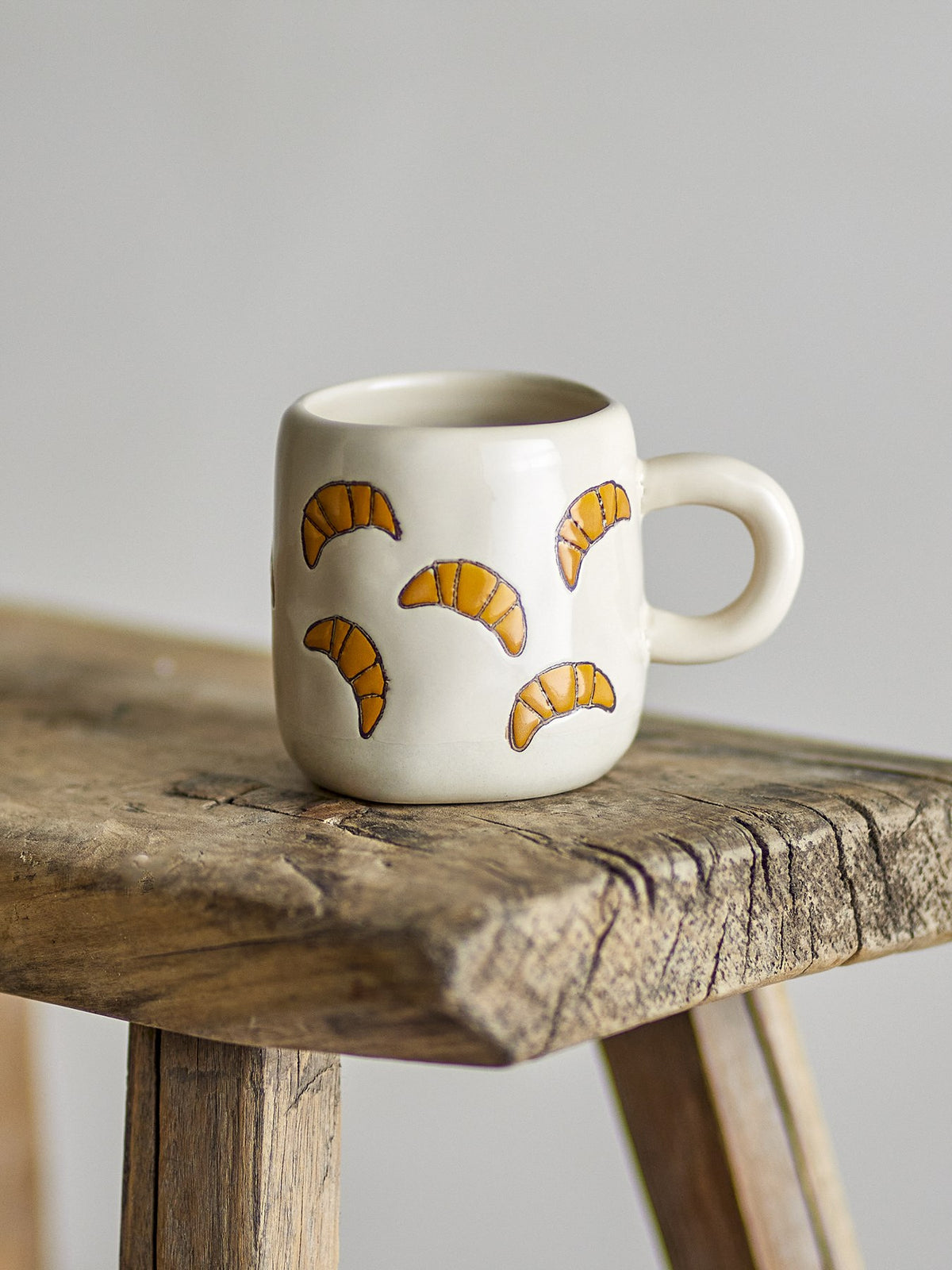 Millie Tasse von Bloomingville Mini aus Steingut, handbemalt mit Croissant-Motiven in Orange, Beige und Grün, kleine runde Form.