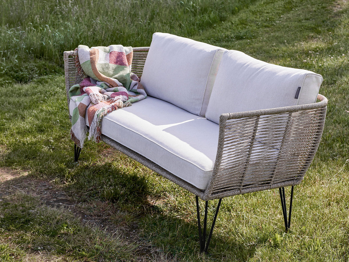 Braunes Lounge Sofa mit Flechtoptik, schwarzem Eisengestell und hellen Kissen, Modell Mundo von Bloomingville im Aussenbereich.
