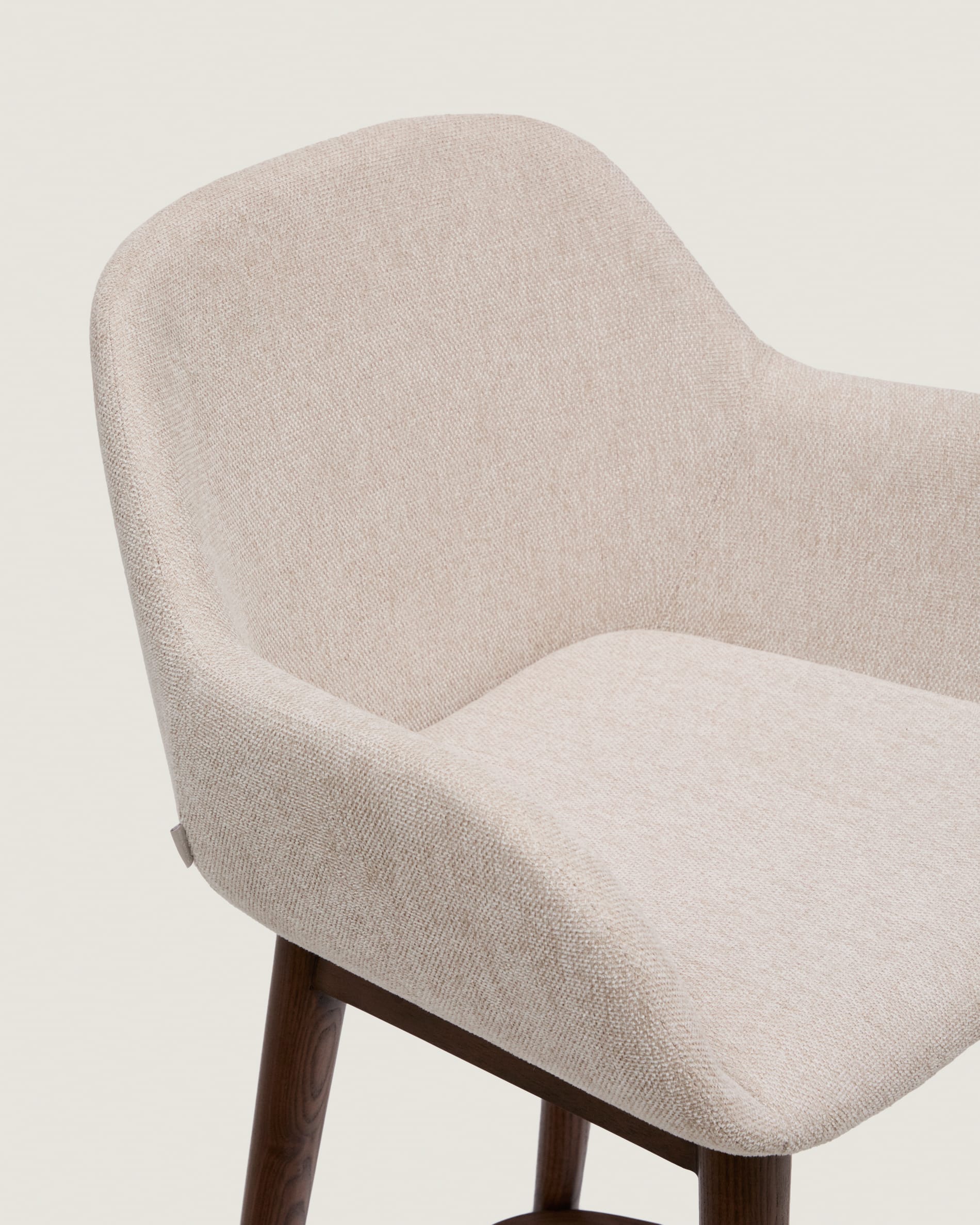 Eleganter Hocker Konna in Beige, 65 cm hoch, mit stabilen Eschenholzbeinen im dunklen Finish. Ideal für moderne Küchen und Essbereiche.