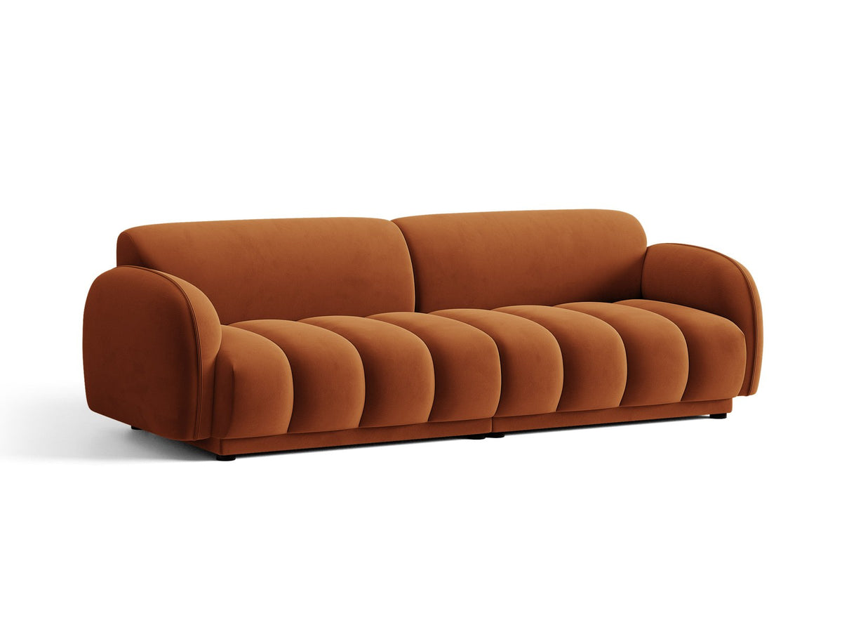 Vierersofa Bilbao mit hellbeigem Samtbezug, schwarzen Kunststoffbeinen und klarer, gerader Linienführung, fotografiert freistehend im Raum.