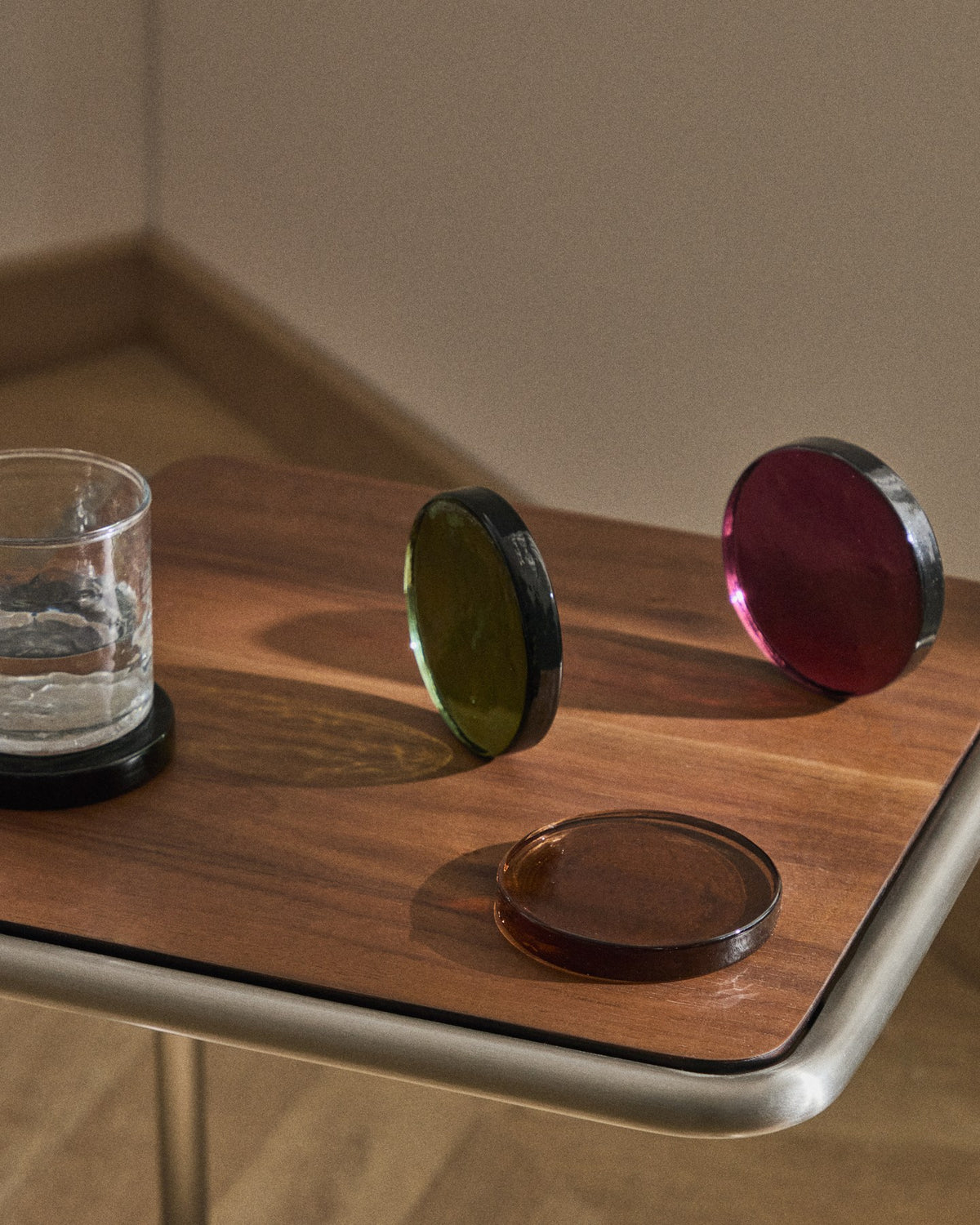 Vier quadratische Untersetzer aus mehrfarbigem Recyclingglas, schlichtes Design, gestapelt auf einer Fläche mit changierenden Farbtönen.