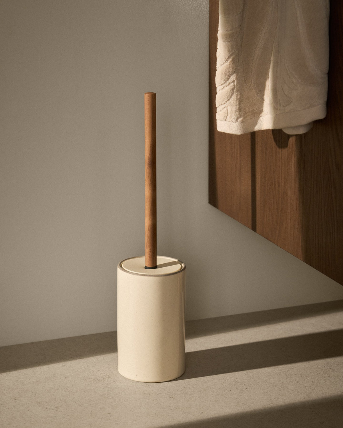 Foto einer schlanken Toilettenbürste aus glasiertem Steingut in Ecru mit Griff und Halter, Material teils Eisen und Polypropylen.