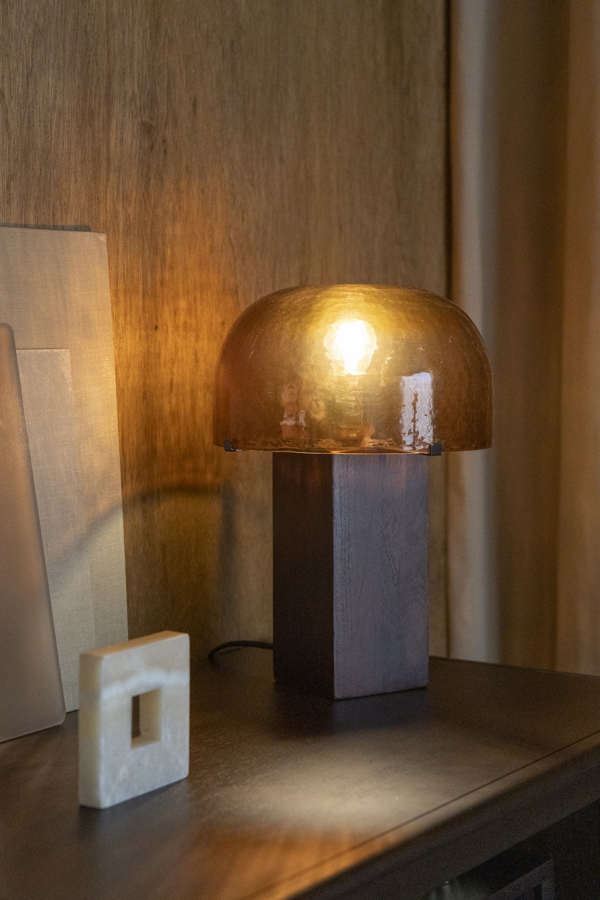 Tischleuchte Mavery Brown von Dutchbone mit rechteckigem Akazienholz-Fuss und halbrundem Glas-Lampenschirm in Pilzform.