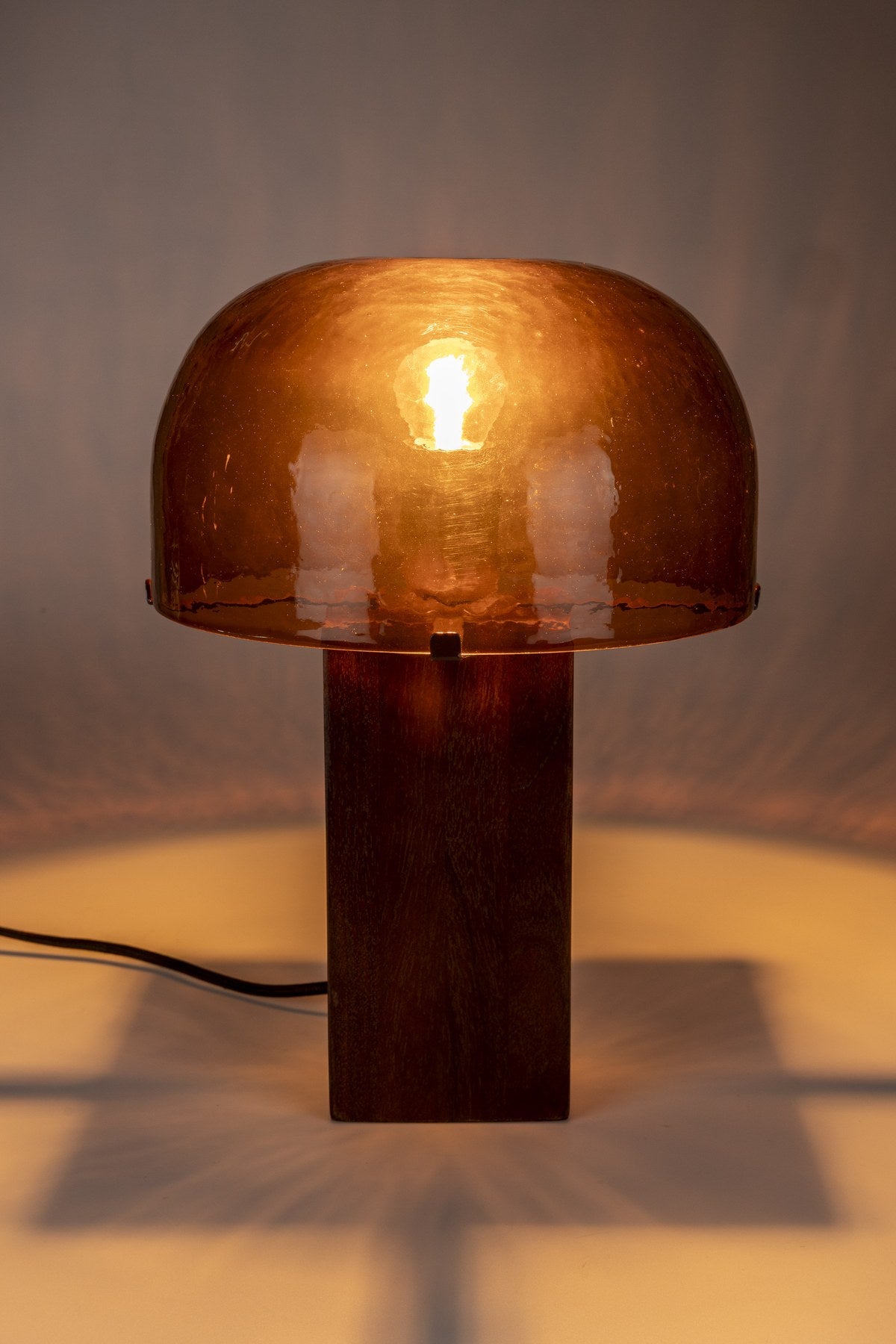 Tischleuchte Mavery Brown von Dutchbone mit rechteckigem Akazienholz-Fuss und halbrundem Glas-Lampenschirm in Pilzform.