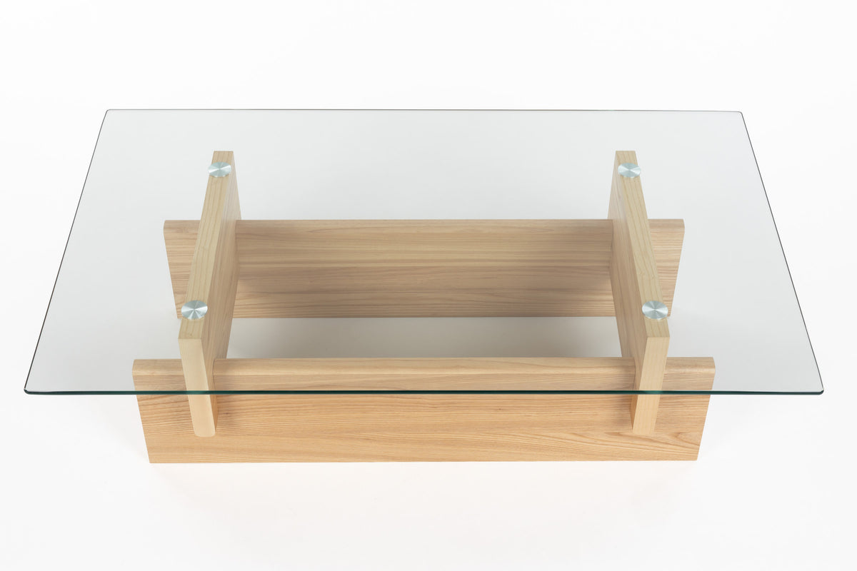 Couchtisch Lucifer Natural von Dutchbone mit Gestell aus zwei quer angeordneten Holzplatten und rechteckiger Tischplatte aus transparentem Glas.