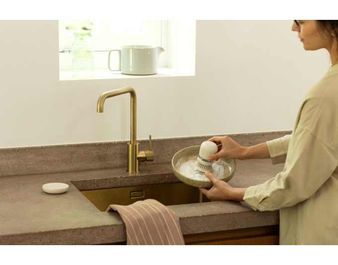 Beige Abwaschbürste mit weissem Seifenspender aus Kunststoff, Polyesterborsten und passendem Ständer auf hellem Untergrund.
