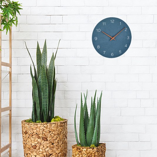 Runde Wanduhr mit taubenblauem MDF-Ziffernblatt, Zeigern aus Walnussholz und schlichtem Rahmen, an heller Wand montiert.