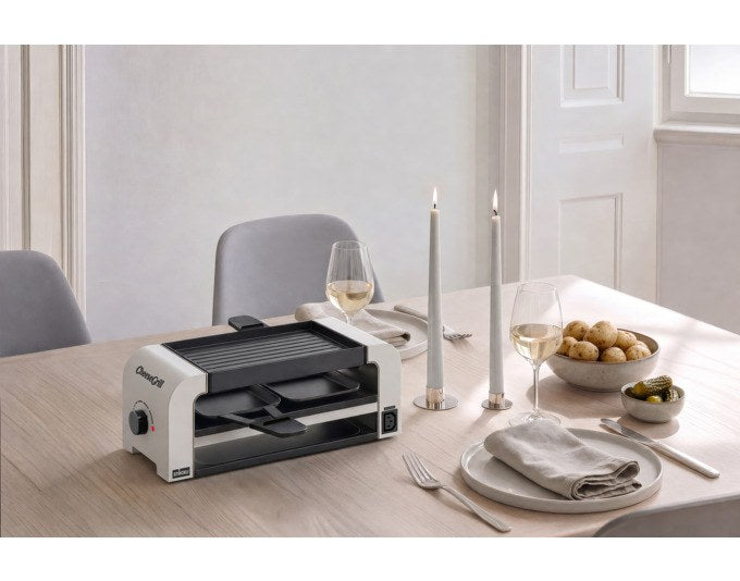 Weisser Tischgrill STÖCKLI CheeseGrill 2 Connect mit wendbarer Aluguss-Grillplatte, zwei Pfännchen und Kunststoffspachtel auf hellem Untergrund.