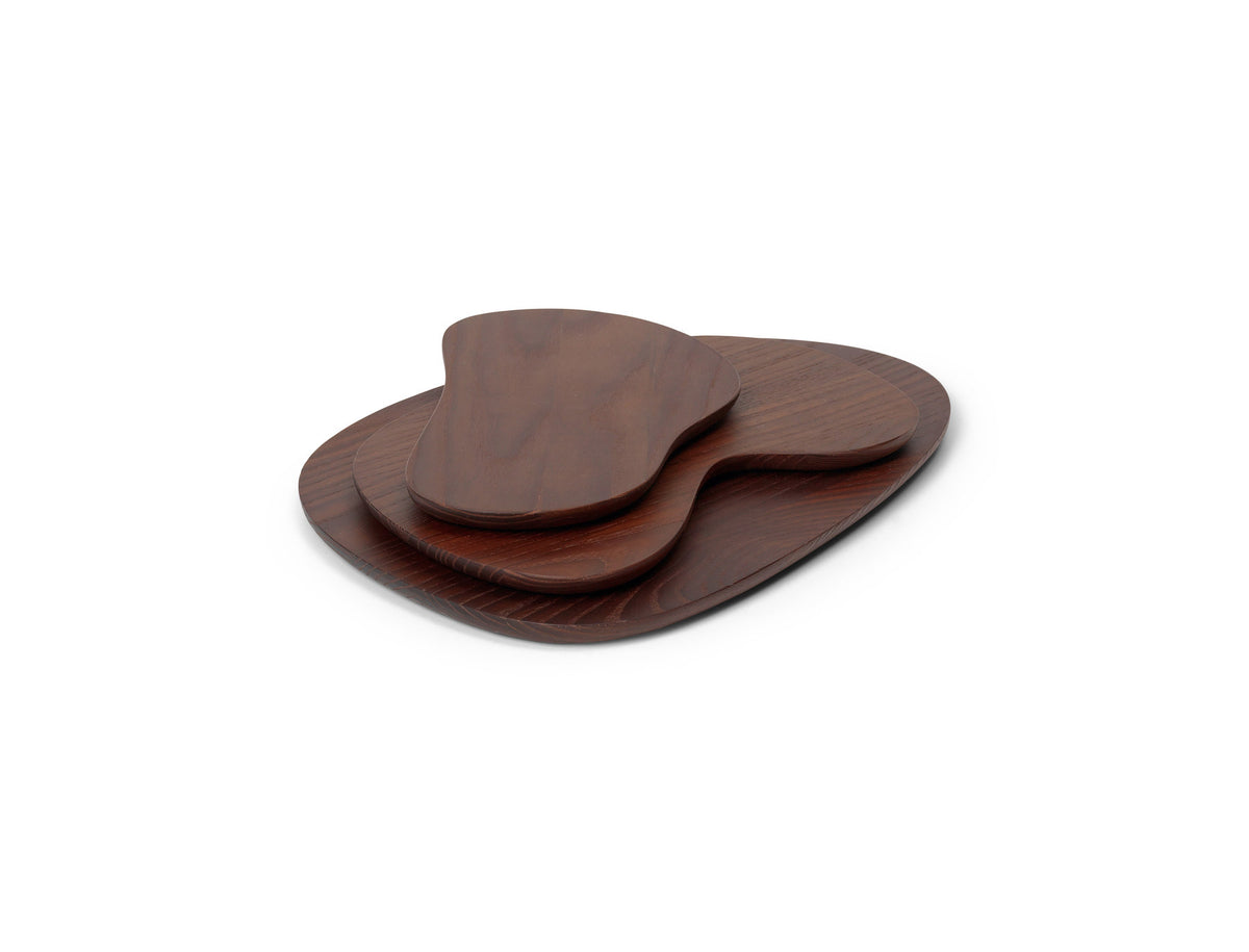 Drei Schneidebretter der Serie Cairn von Ferm Living aus dunkelbraunem, karbonisiertem Eschenholz mit organischen, abgerundeten Formen auf hellem Hintergrund.