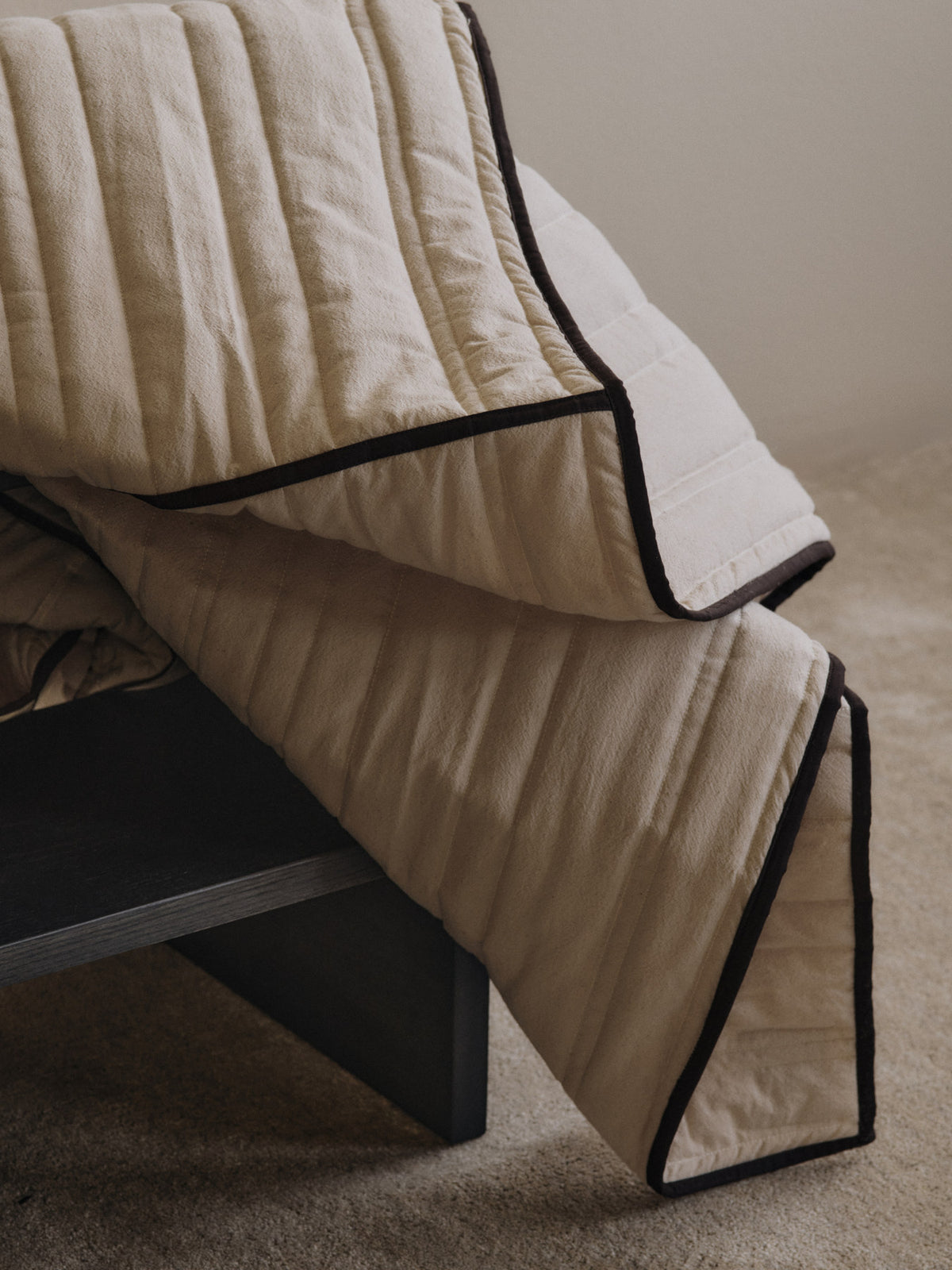 Gesteppte Tagesdecke Vari von Ferm Living aus Bio-Baumwolle in Natural mit Paspelierung in Dark Chocolate, auf Bett drapiert.