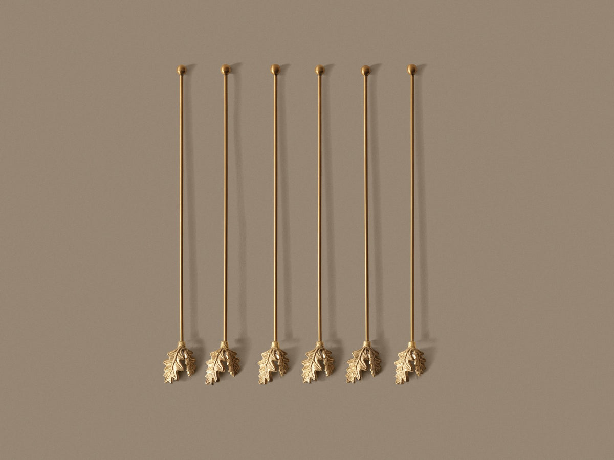 Sechs schlanke Rührstäbchen aus Messing mit Edelstahlkern, Griffe in Eichenblattform, Länge 24 cm, Durchmesser 0.3 cm.