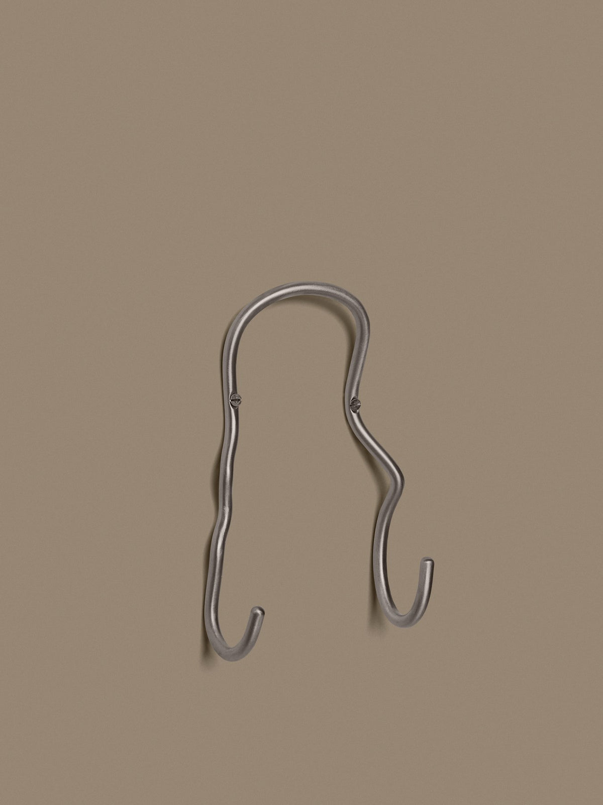 Doppelhaken Curvature von Ferm Living aus Edelstahl mit geschwungener, skulpturaler Form, montiert an einer Wand.