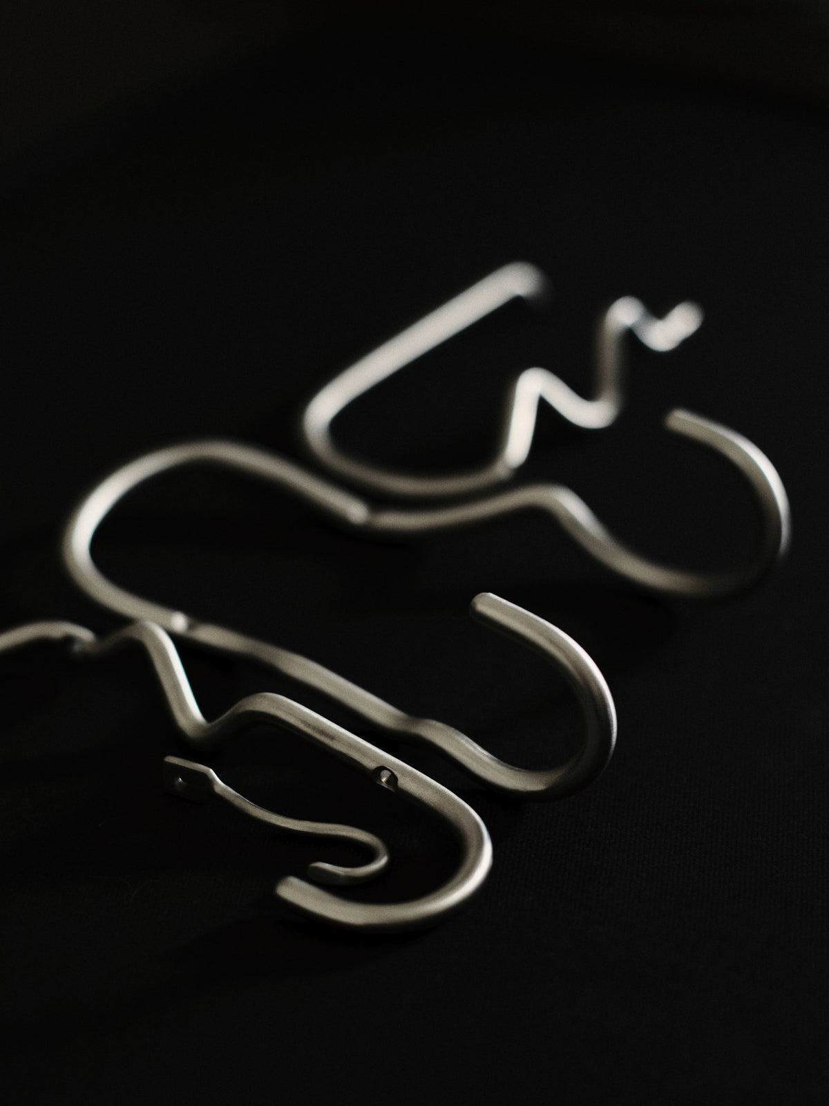 Doppelhaken Curvature von Ferm Living aus Edelstahl mit geschwungener, skulpturaler Form, montiert an einer Wand.