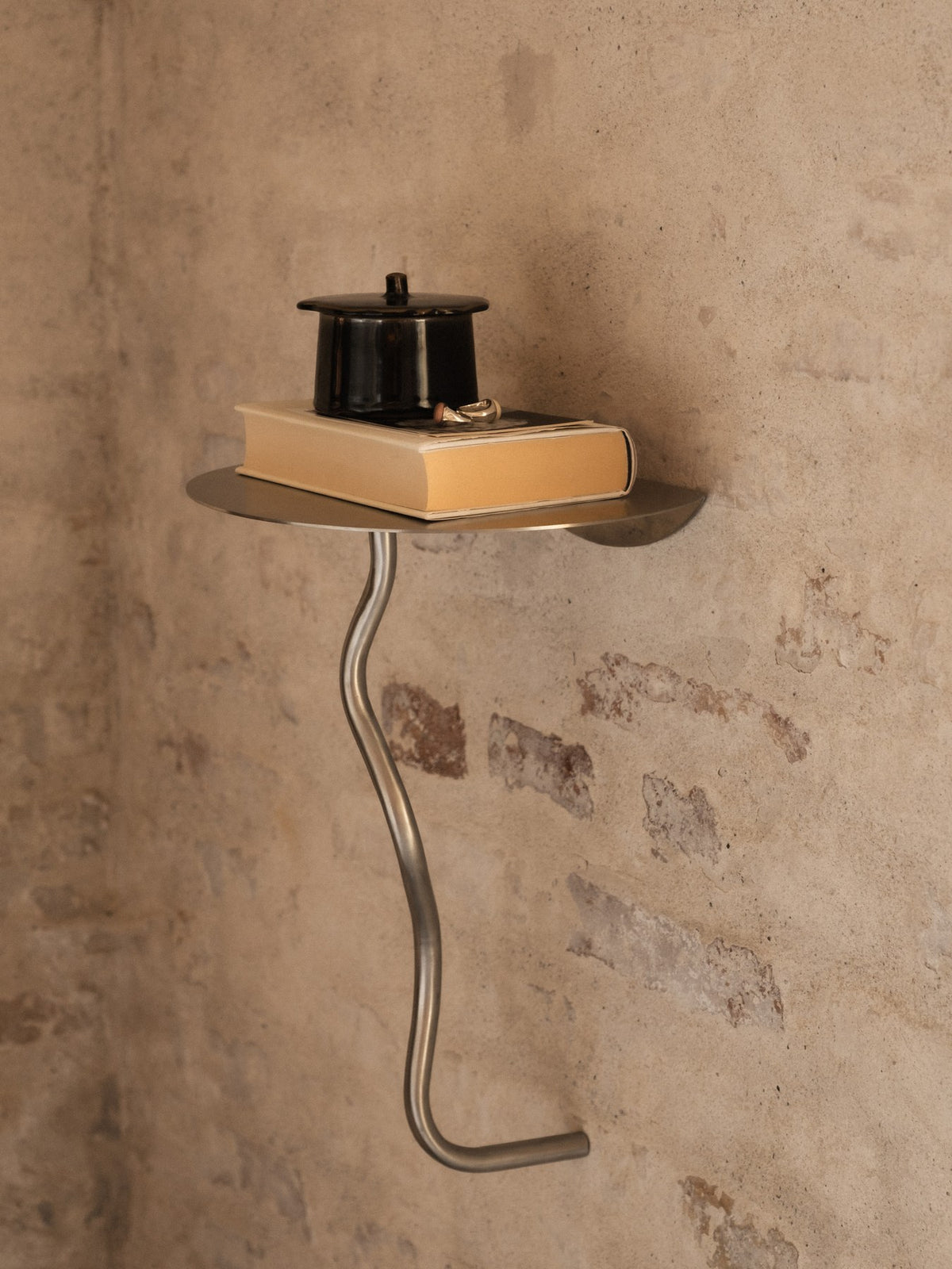 Wandmontierter Beistelltisch Curvature von Ferm Living aus Edelstahl mit geschwungener Form, kompakte Ablagefläche für den Wohnbereich.