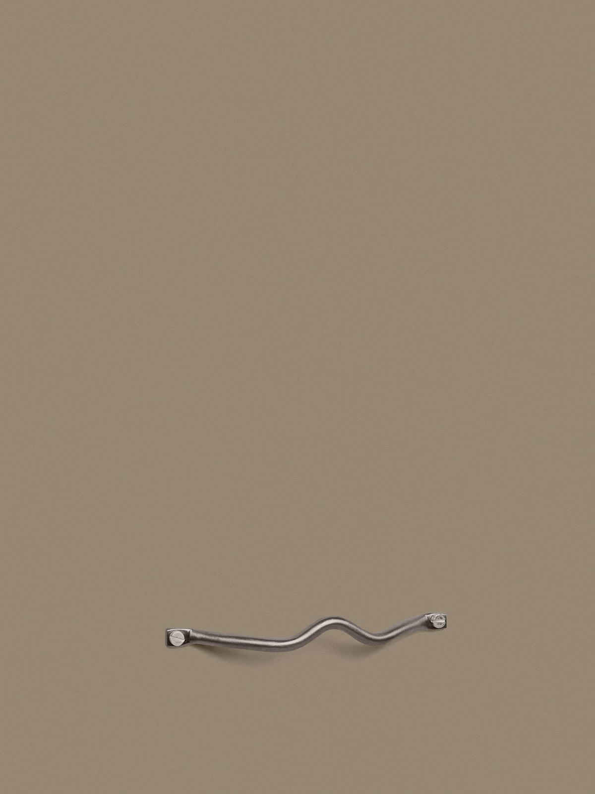 Curvature Handgriff von Ferm Living aus Edelstahl mit organisch geschwungener Form, montiert an einer Schrank- oder Schubladenfront.