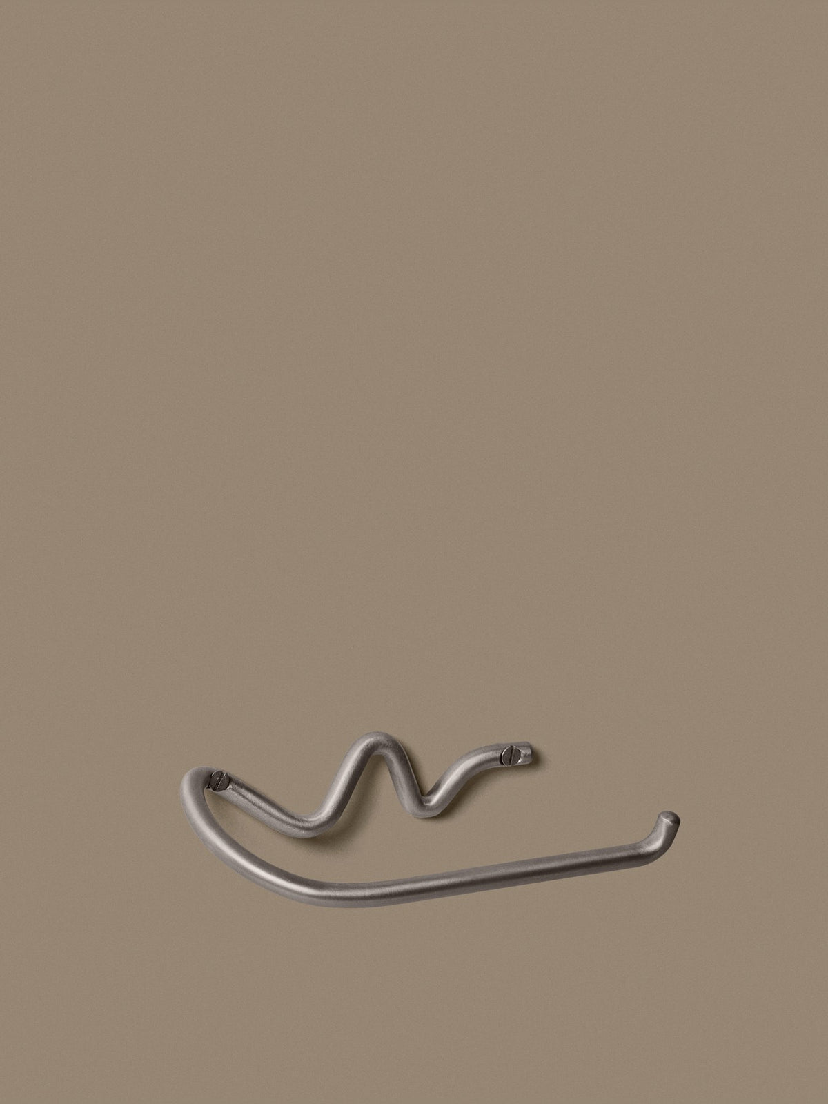 Wandmontierter Toilettenpapierhalter aus Edelstahl mit geschwungener, skulpturaler Form, handgefertigt von Ferm Living für das Badezimmer.