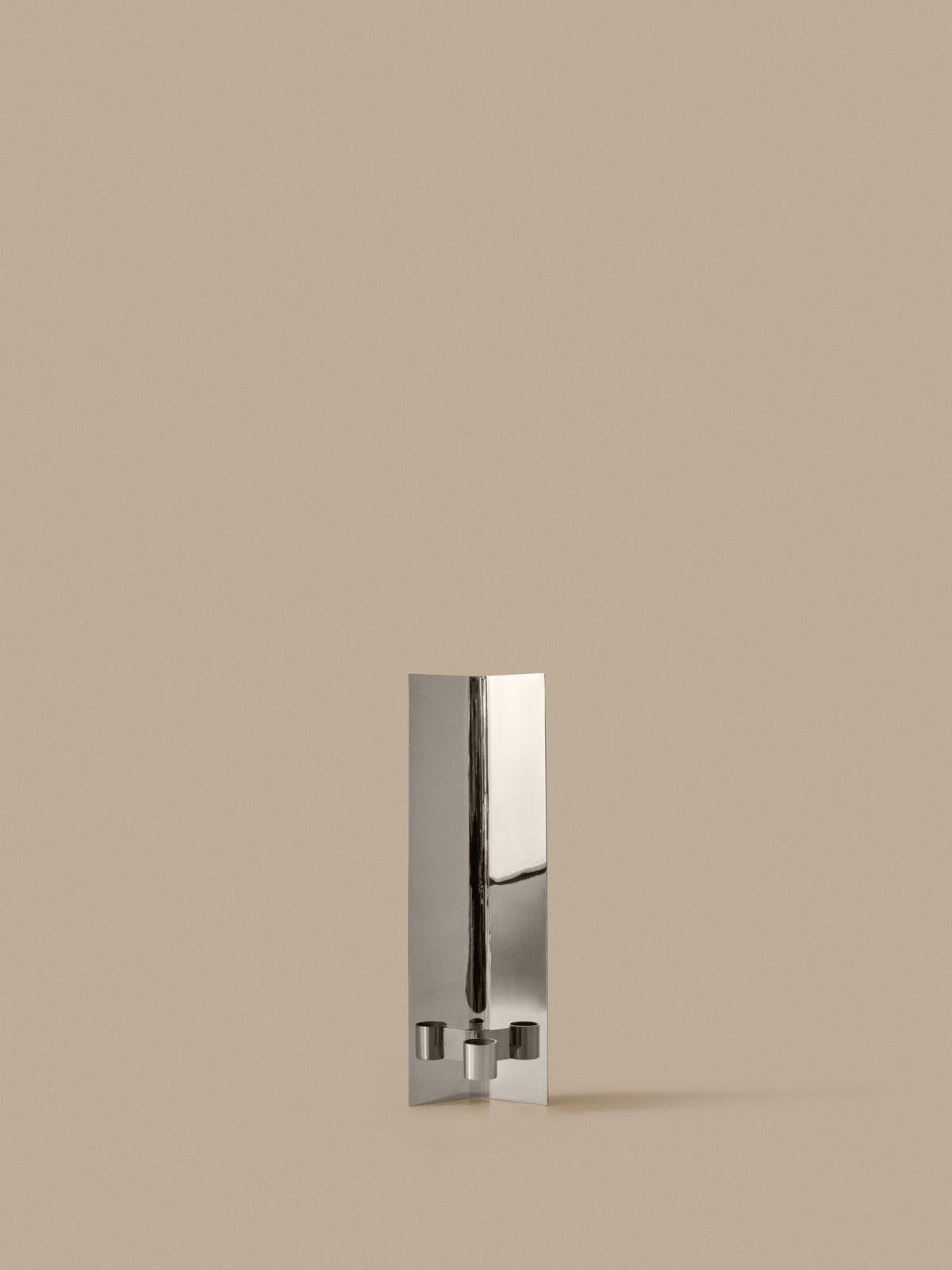 Eddy Wandkerzenhalter von Ferm Living aus spiegelpoliertem Edelstahl, schlichte gefaltete Form, montiert an weisser Wand.