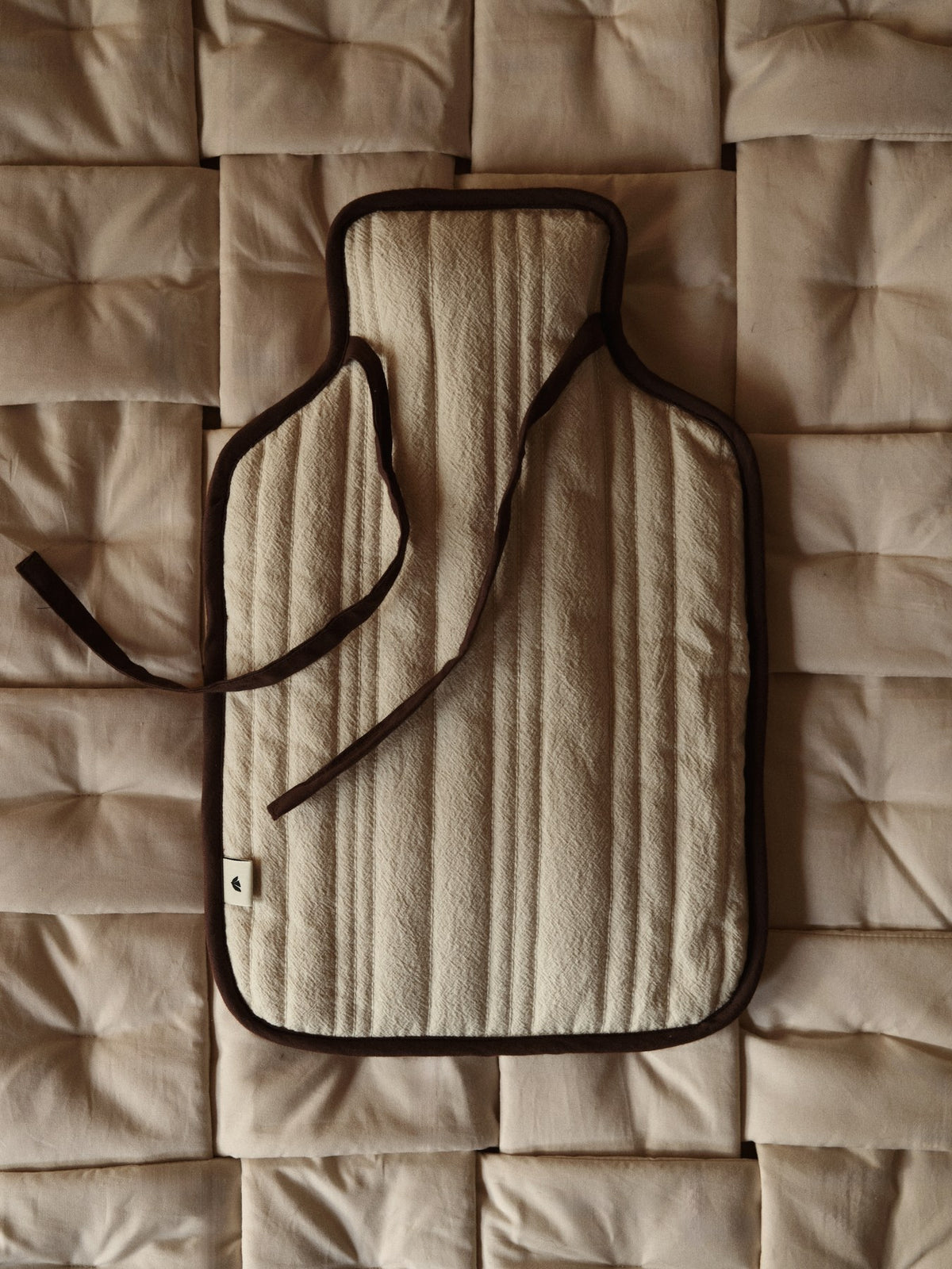 Wärmflaschenbezug aus gesteppter Bio-Baumwolle in Natur mit dunkelbraunem Kantenband und Perlmuttknopf-Verschluss, Ferm Living Design.