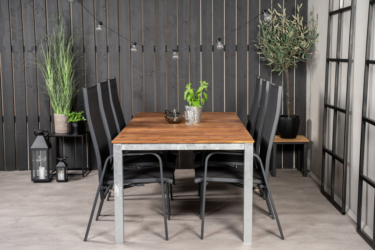Zwei schwarze Relaxsessel aus Akazie und Stahl neben einem rechteckigen Esstisch mit Akazie-Tischplatte in Natur und Aluminiumbeinen.