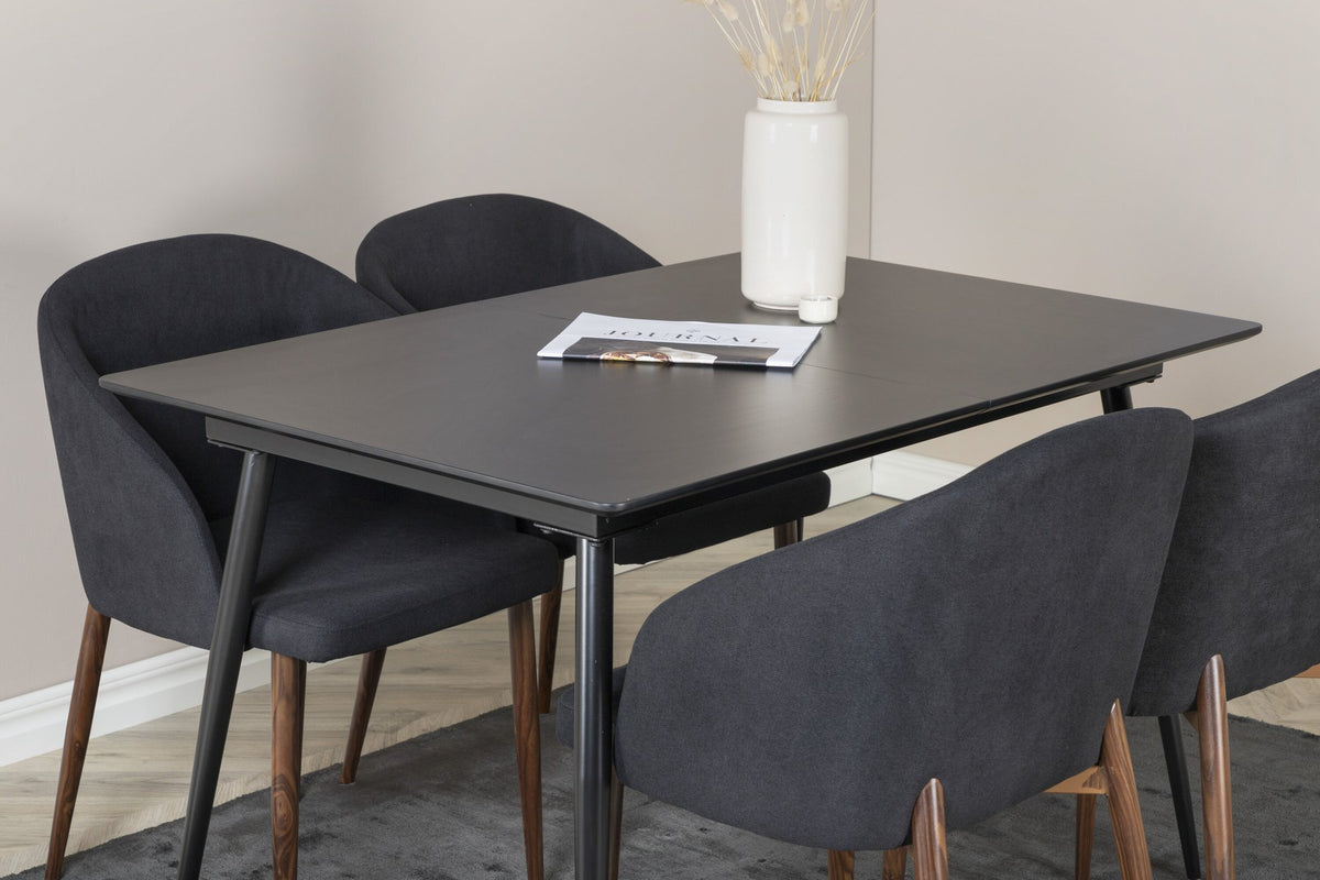 Rechteckiger Esstisch aus MDF und Stahl in Schwarz mit ausziehbarer Platte, daneben zwei Stühle mit Walnussbeinen und schwarzem Stoffbezug.