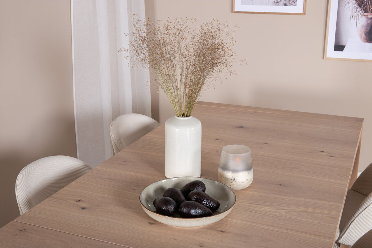 Esstisch mit heller Holzplatte in Naturfarbton auf Eichen-Gestell, umgeben von cremefarbenen Polsterstühlen aus Samt der Velvet-Serie.