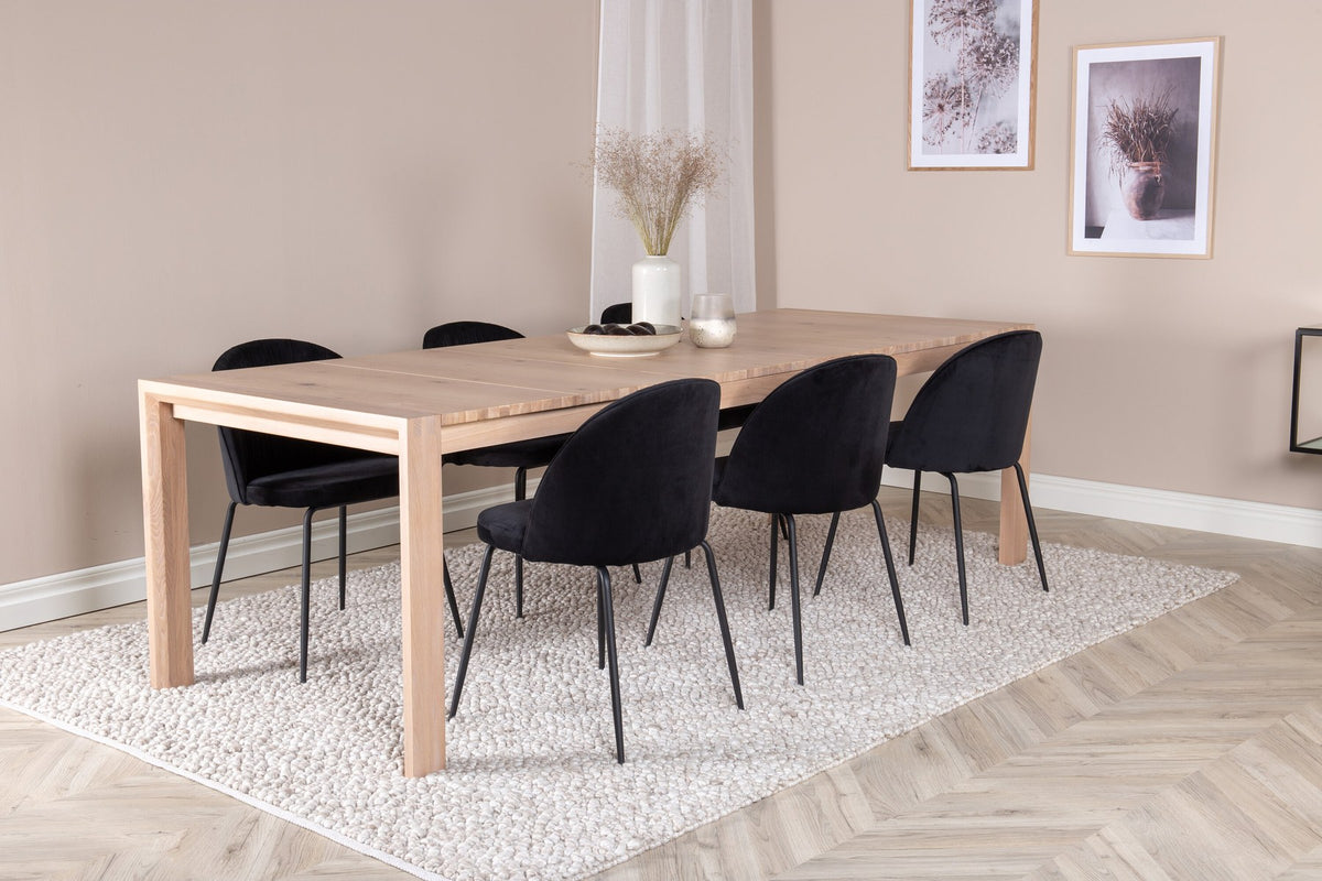 Rechteckiger Esstisch aus Eiche mit weissgelaugter Tischplatte, kombiniert mit zwei schwarzen Esszimmerstühlen im skandinavischen Design.