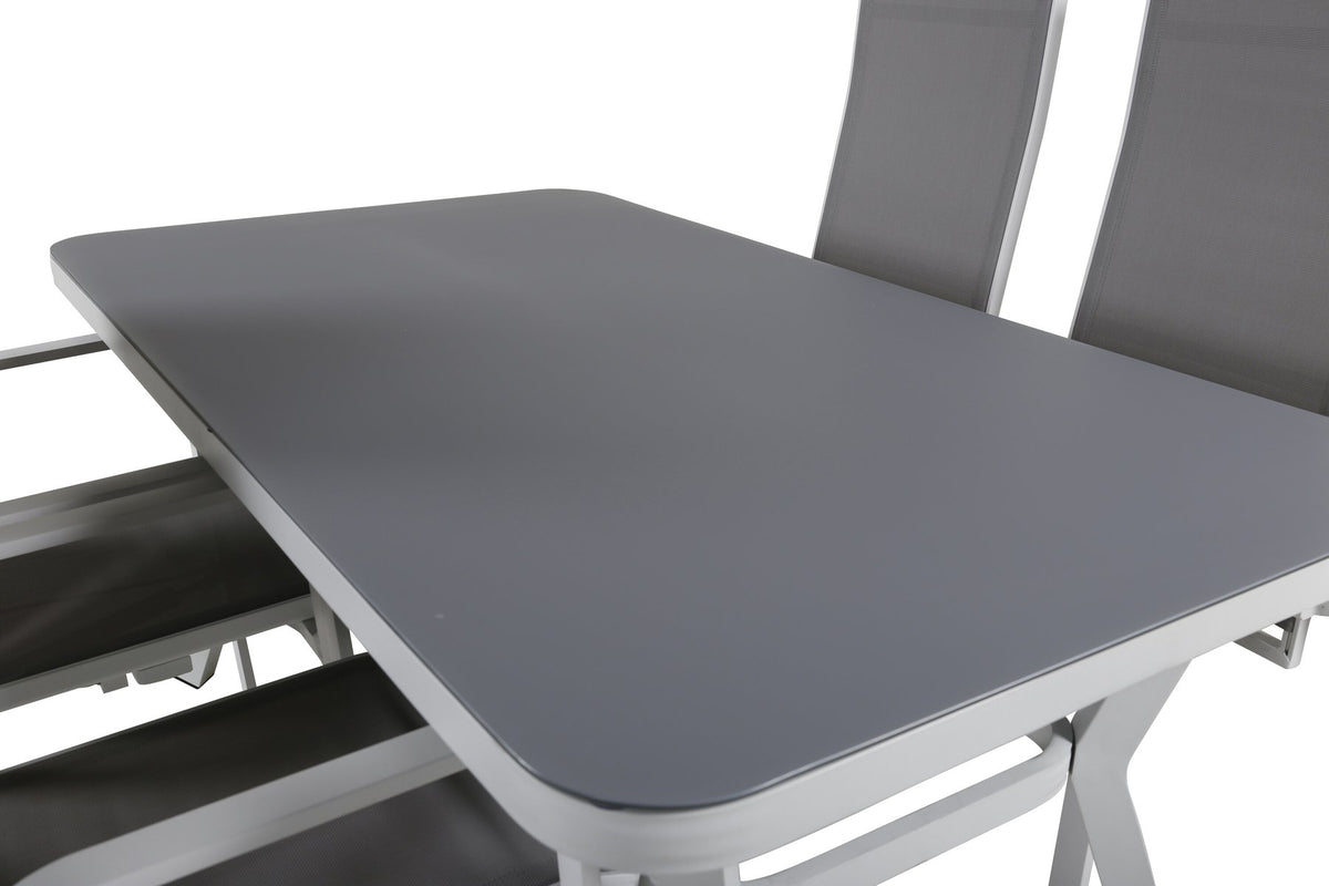 Rechteckiger Esstisch mit grauem Gestell und schwarzer Mattglas-Tischplatte, daneben zwei graue Relaxsessel aus Textilene mit Aluminiumbeinen.