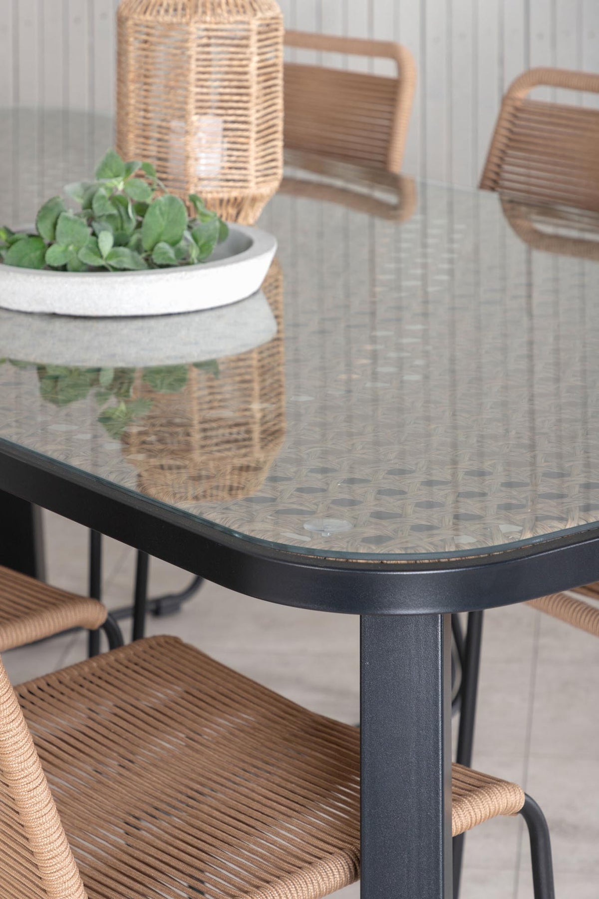 Gartentischset Paola mit schwarzem Stahlgestell und Weidengeflecht-Tischplatte sowie sechs stapelbaren Lindos-Stühlen aus schwarzem Aluminium und Polyesterseil.